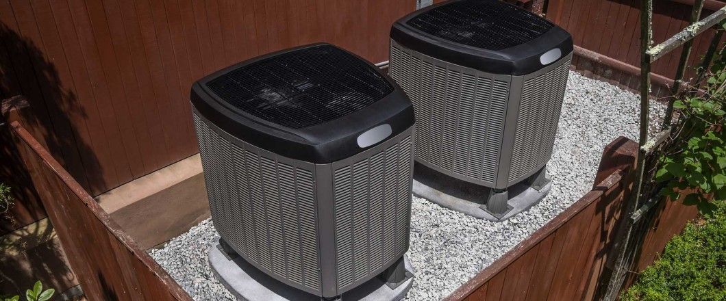 Two air conditioners are sitting on top of a gravel covered roof.