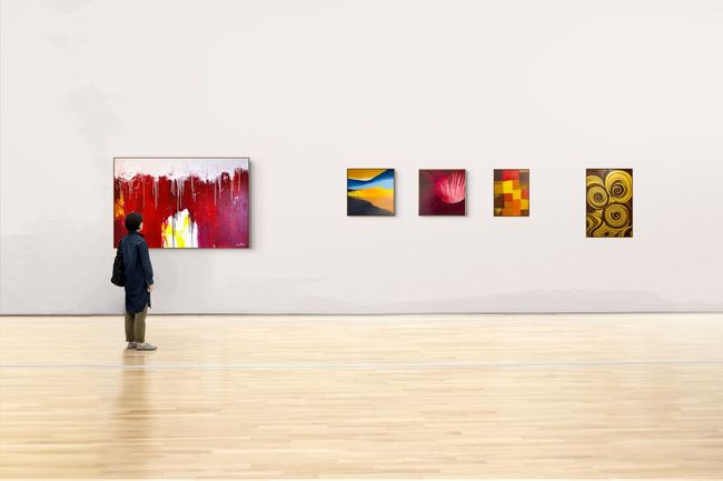 Person viewing colorful abstract paintings in a gallery with a polished wooden floor.