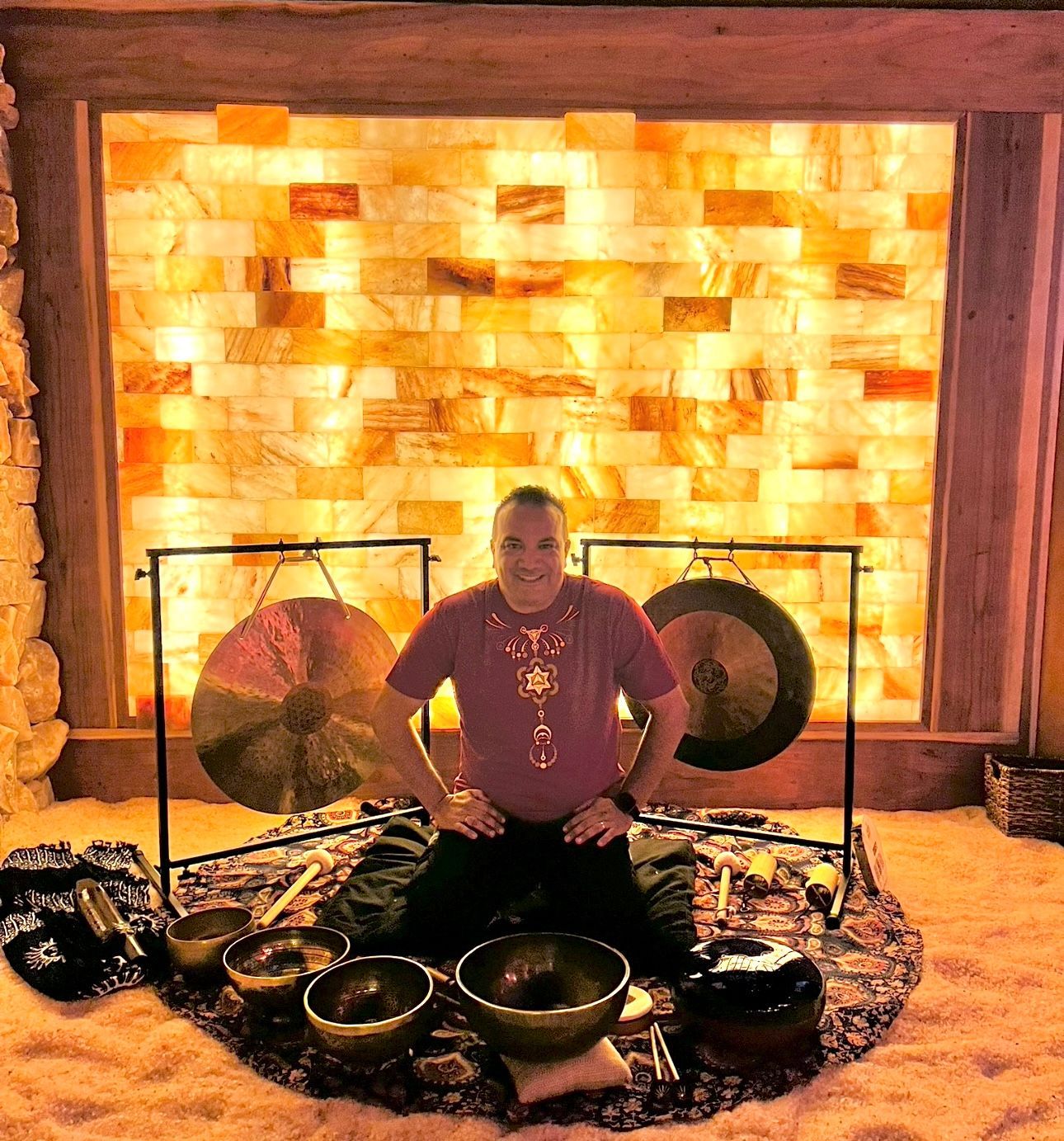 A woman sits cross-legged on floor in front of fireplace with four white sound bath instruments arranged before her