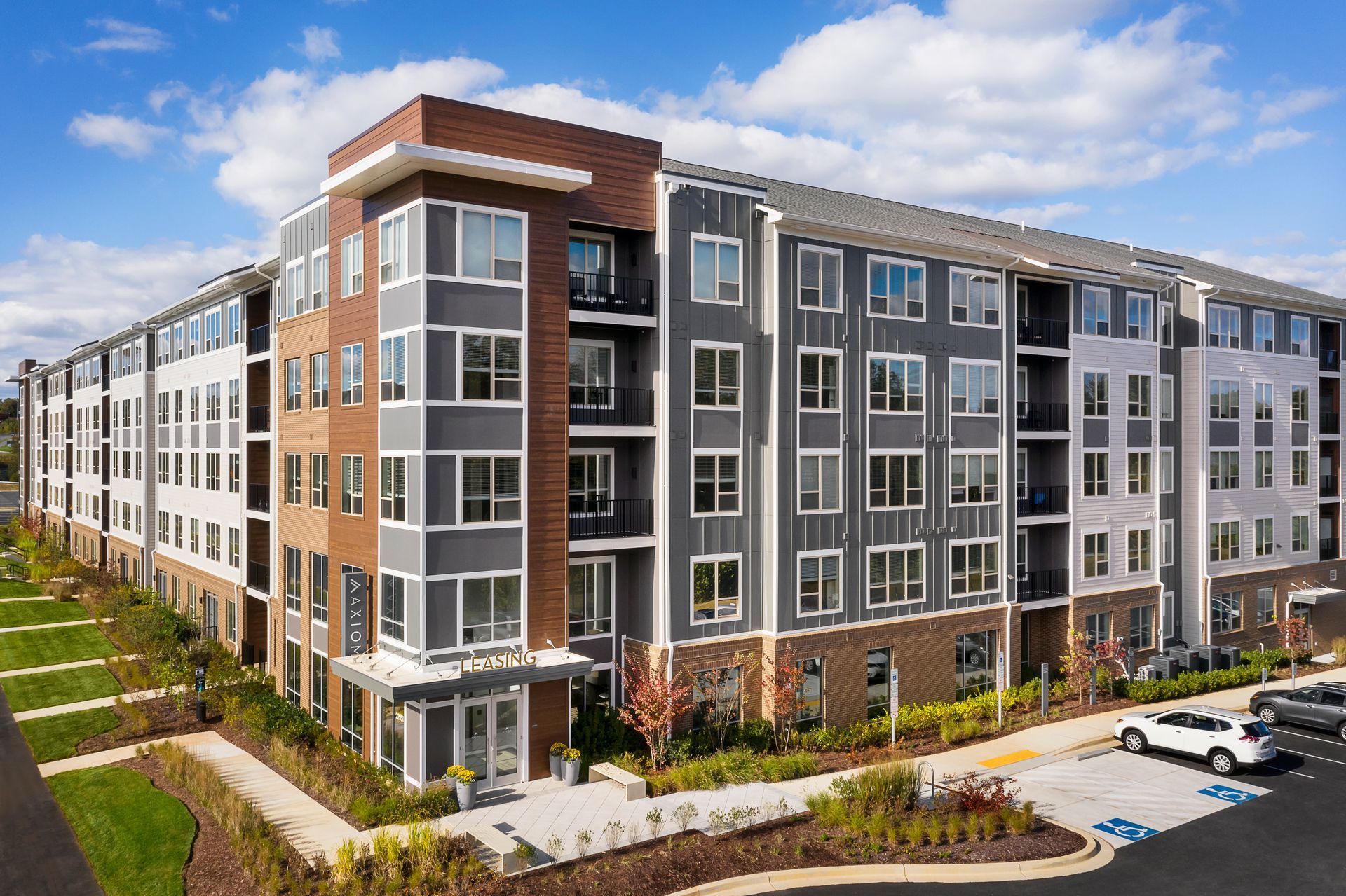 Modern multi-story apartment building with varying shades of gray siding, brown accents, and small balconies.