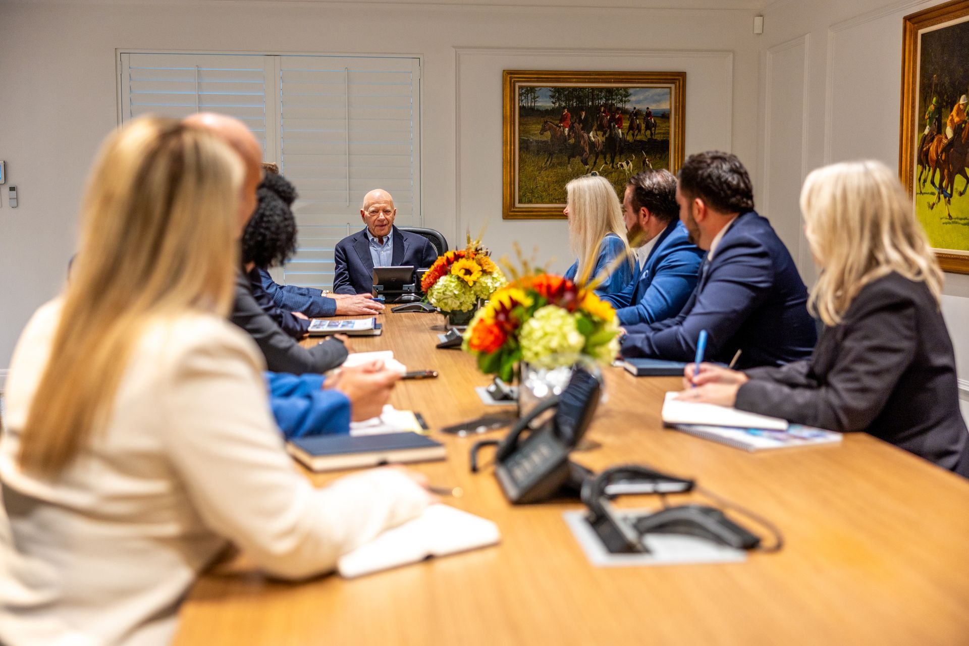 People in business attire at a conference table with documents, flower arrangement.