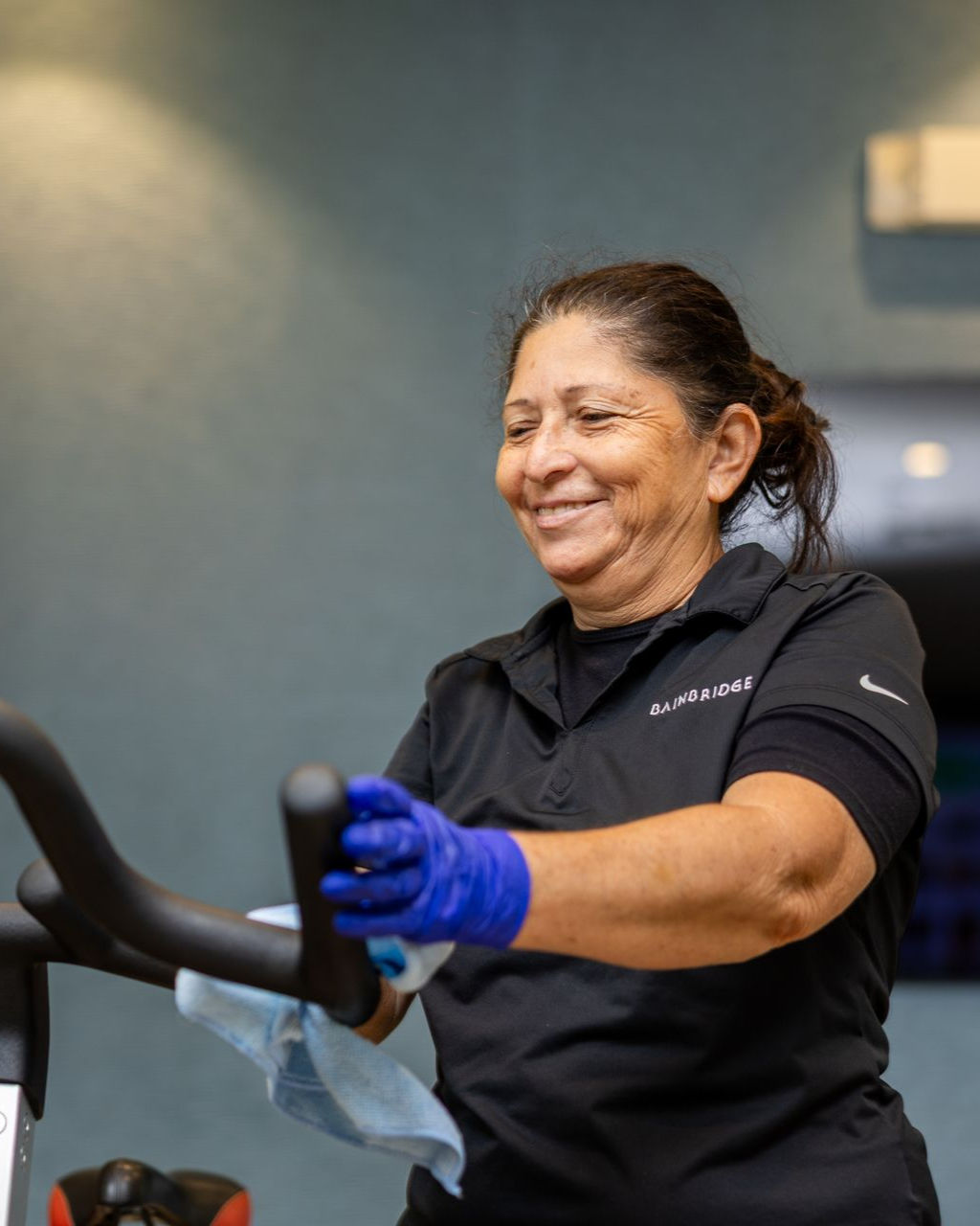 Woman in blue gloves cleaning in a gym, smiling.
