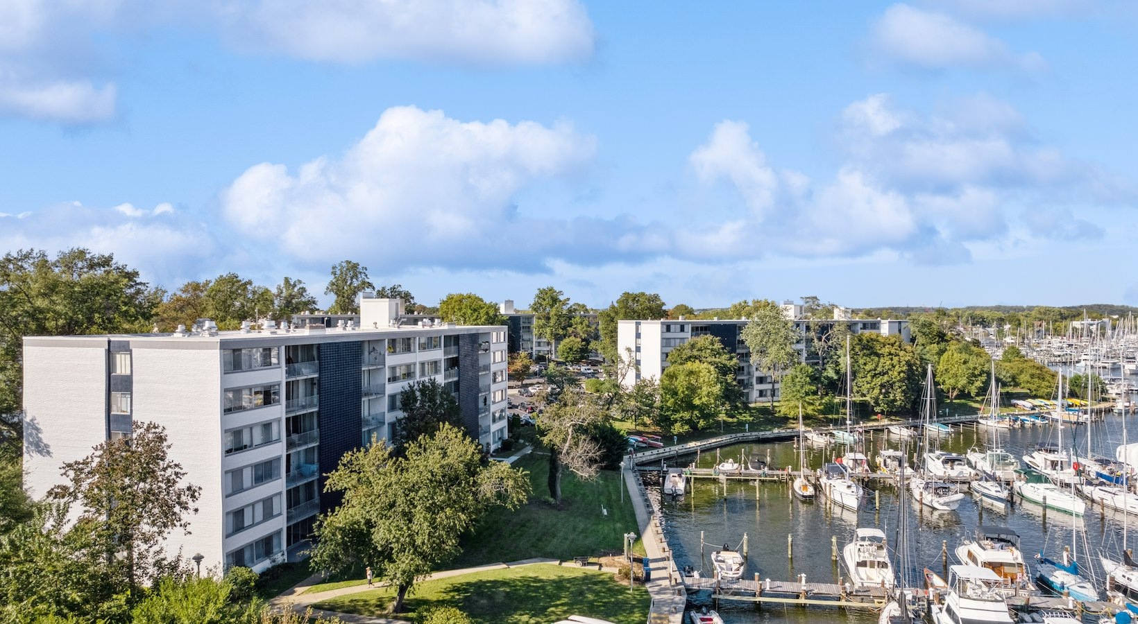 Apartment buildings beside a marina with sailboats under a partly cloudy blue sky