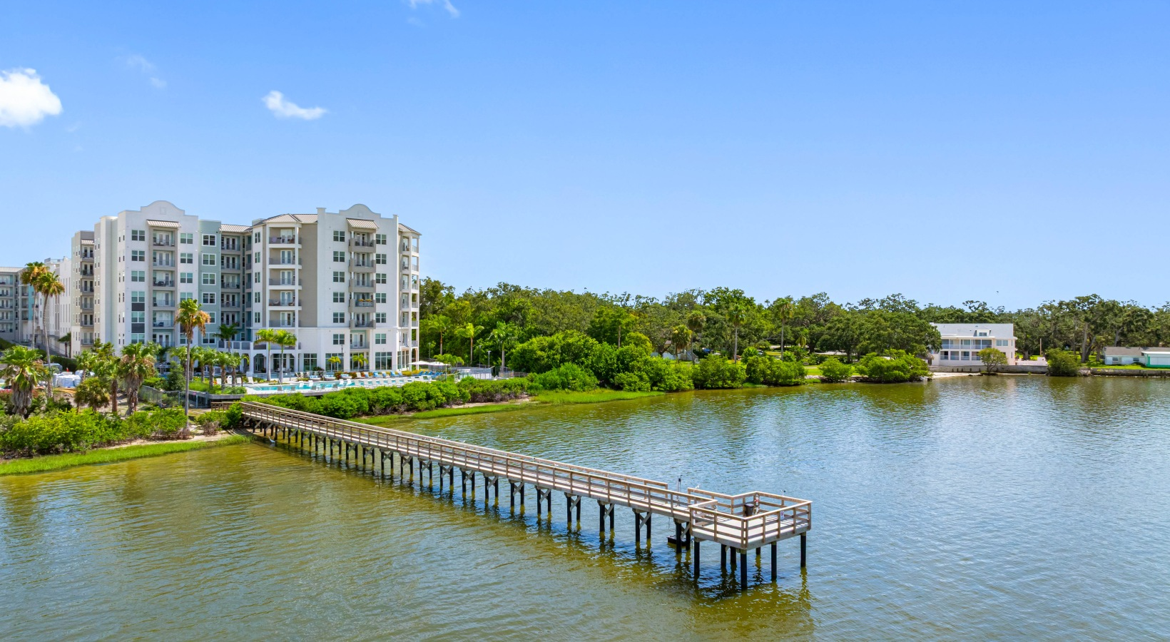 Apartment buildings beside a calm lake with a wooden pier under a clear blue sky