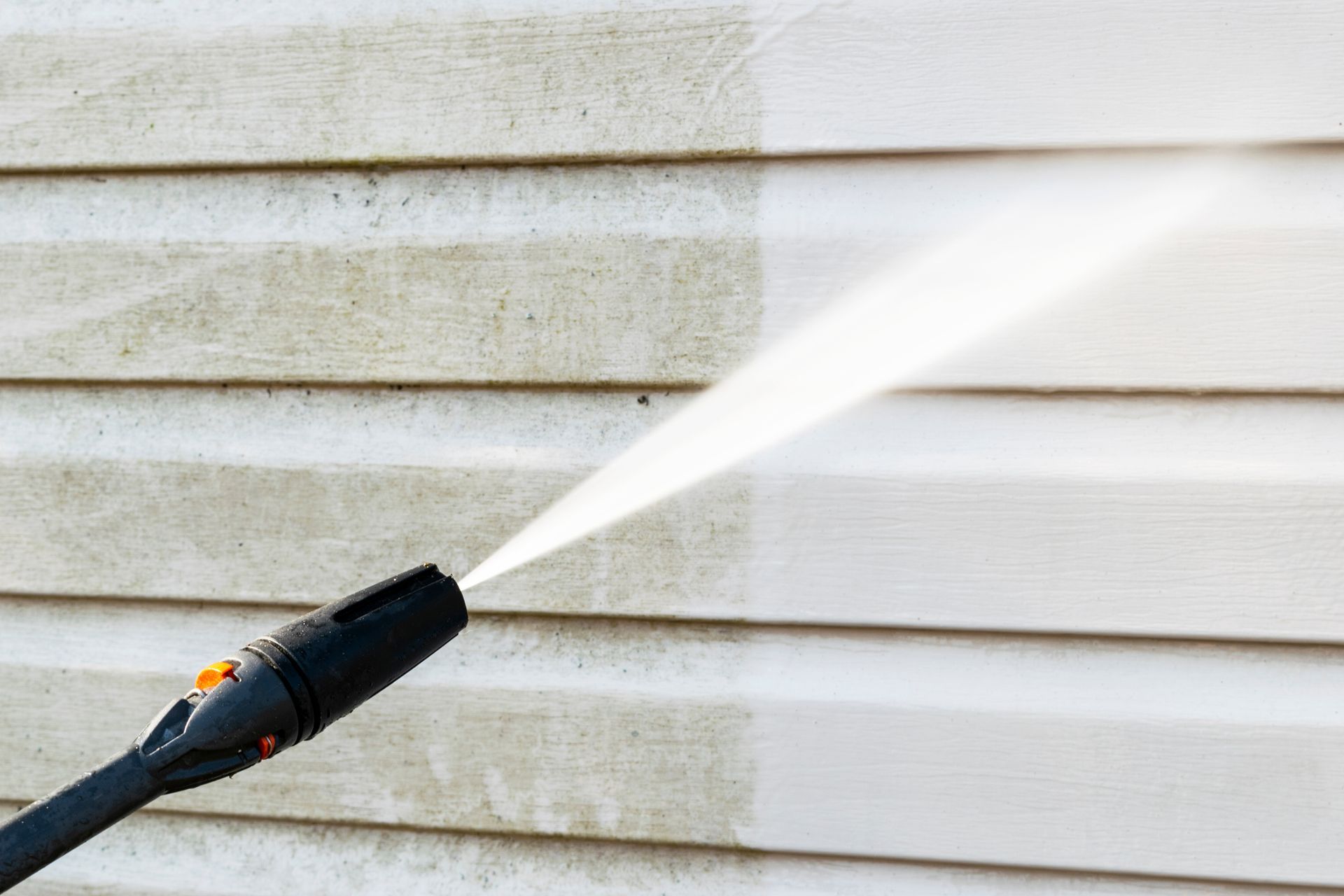 A man is using a high pressure washer to clean the side of a house.