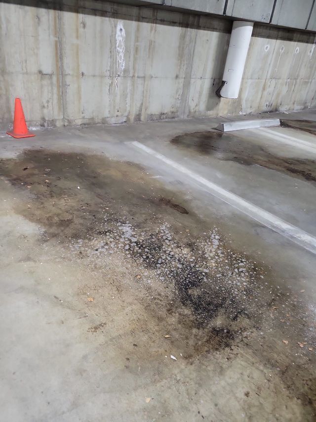 A dirty parking lot with a concrete wall and an orange cone.