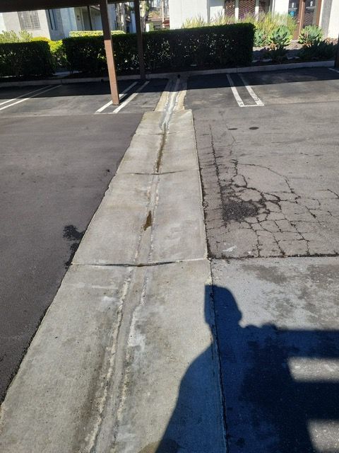 A shadow of a person is cast on a sidewalk next to a parking lot