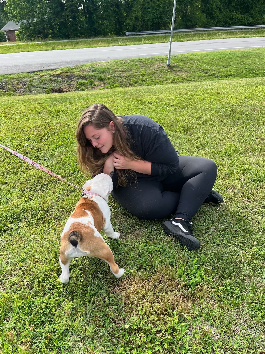 a woman is kneeling on the grass petting a dog .