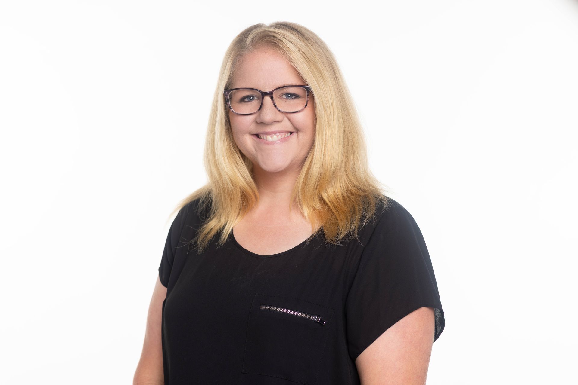 A woman wearing glasses and a black shirt is standing in front of a brick wall.