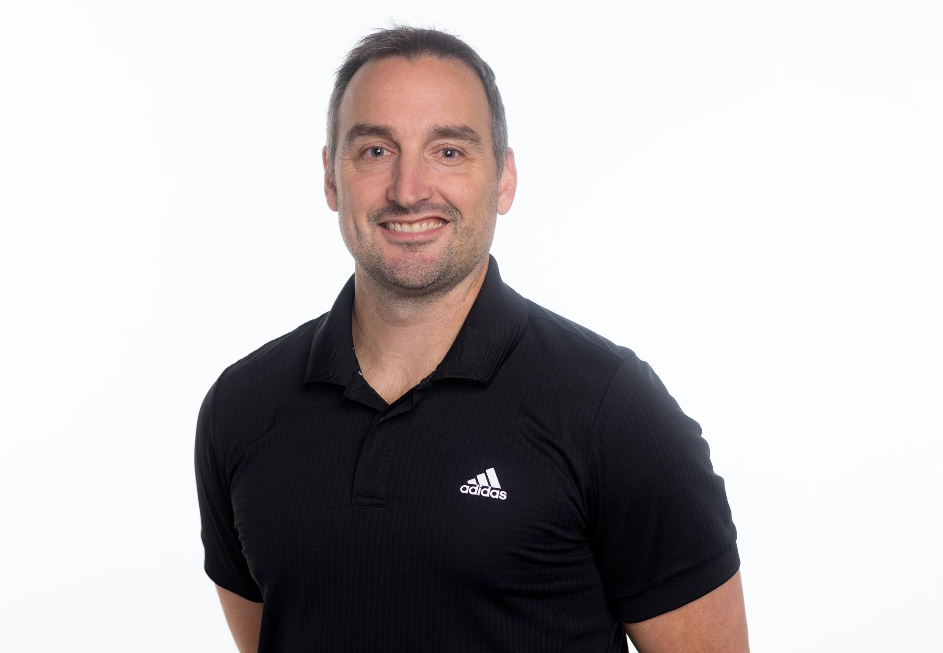 A man in a black adidas polo shirt is smiling for the camera.