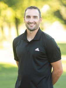 A man in a black adidas polo shirt is smiling for the camera.