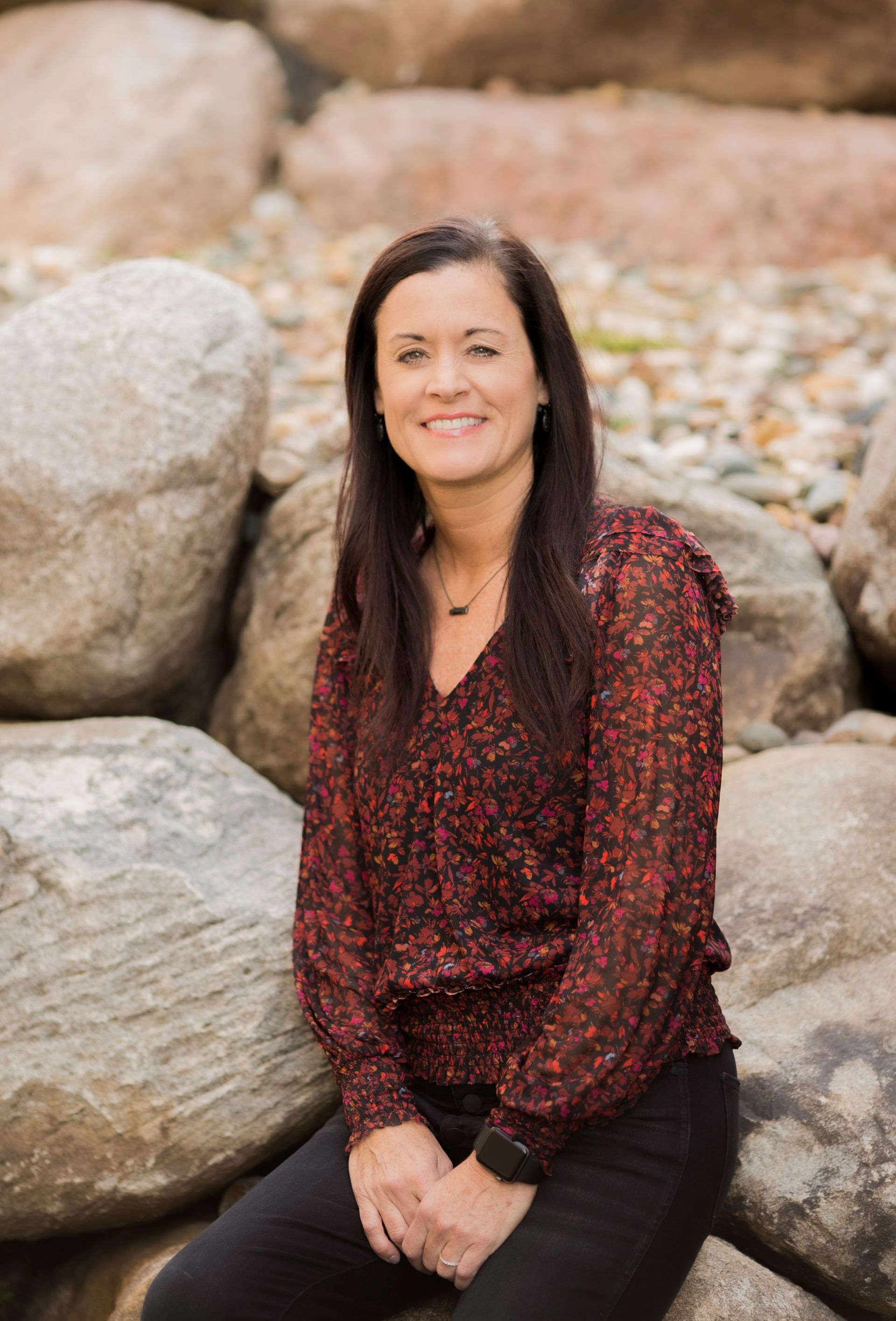 A woman is sitting on a pile of rocks and smiling.