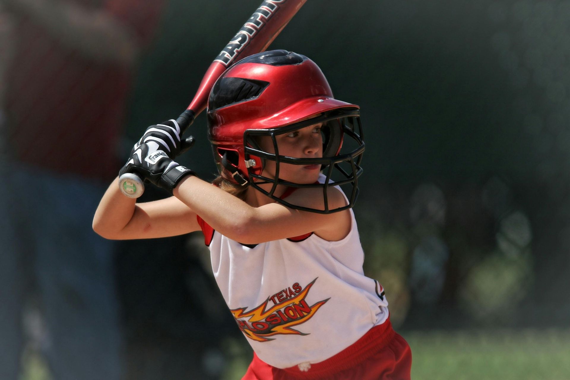 A little girl is holding a bat and wearing a helmet with the word texas on it