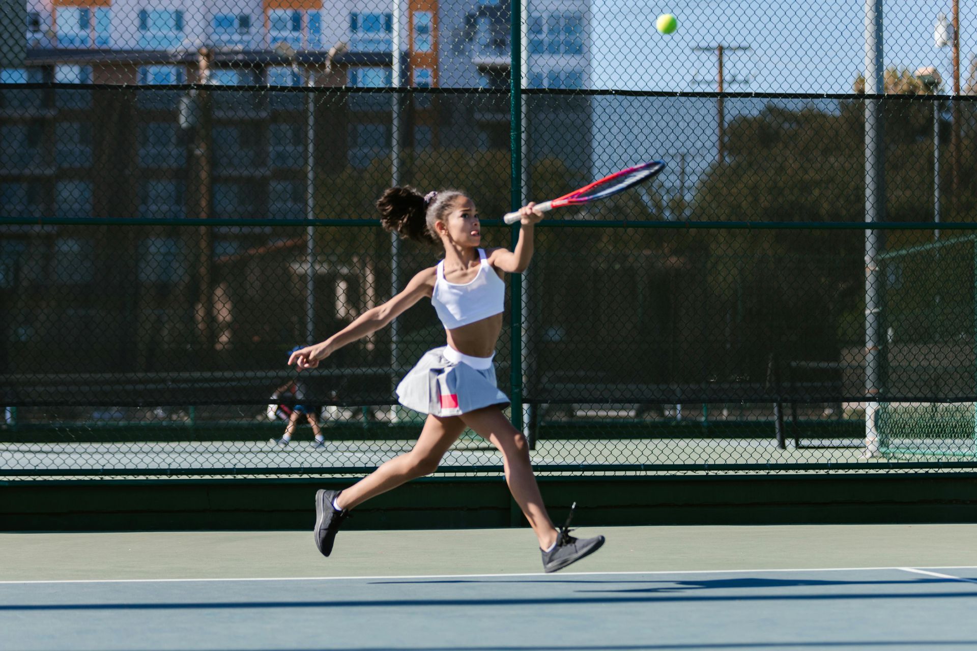 A woman is swinging a tennis racket at a tennis ball on a tennis court.