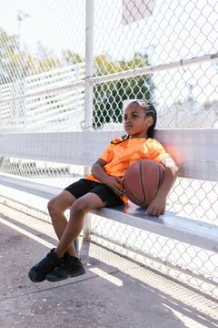 A young girl is sitting on a bench holding a basketball.