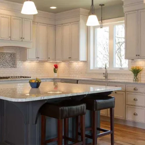 A kitchen with white cabinets , granite counter tops , stools and a large island.