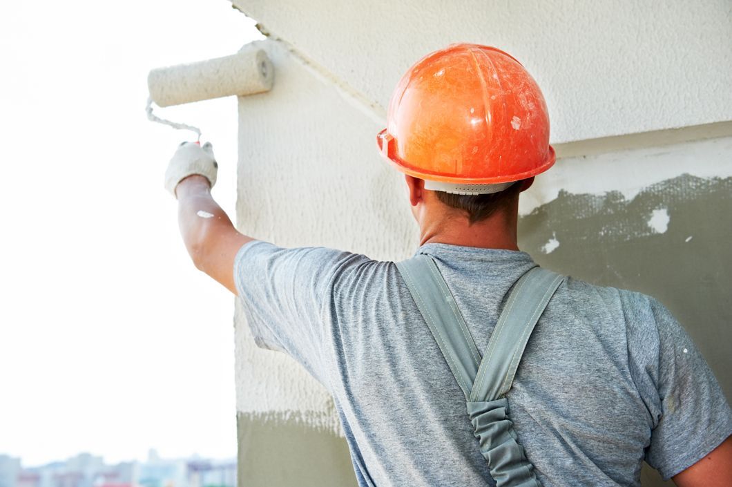A man wearing a hard hat is painting a wall with a roller.