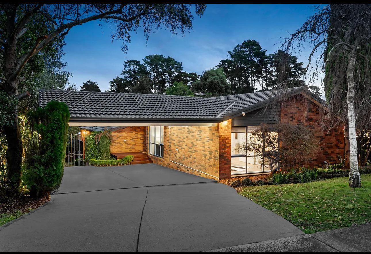 A brick house with a driveway and trees in front of it