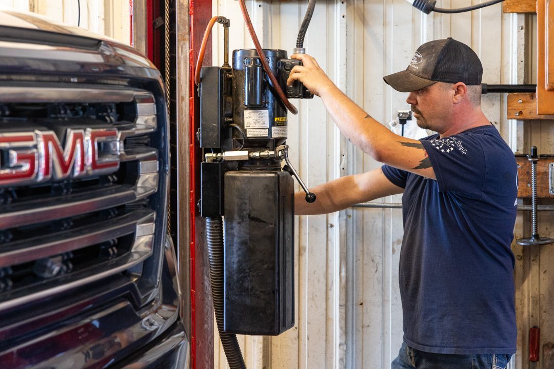 Mechanic working on lift, near a GMC truck in a garage.