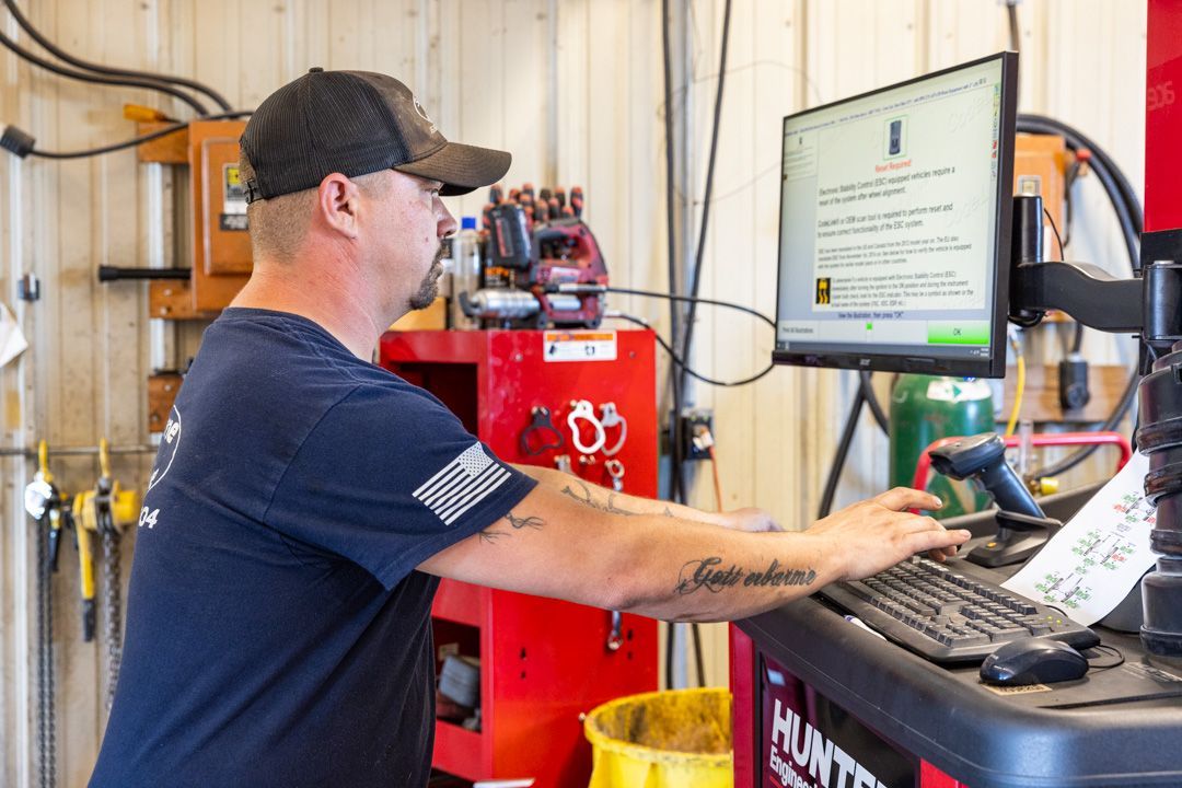 Man in a garage working at a computer, likely checking car diagnostics.