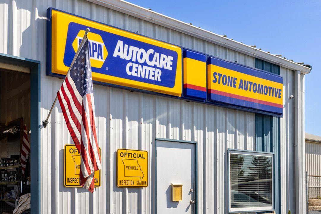 NAPA AutoCare Center and Stone Automotive sign on a light blue building with an American flag hanging outside.
