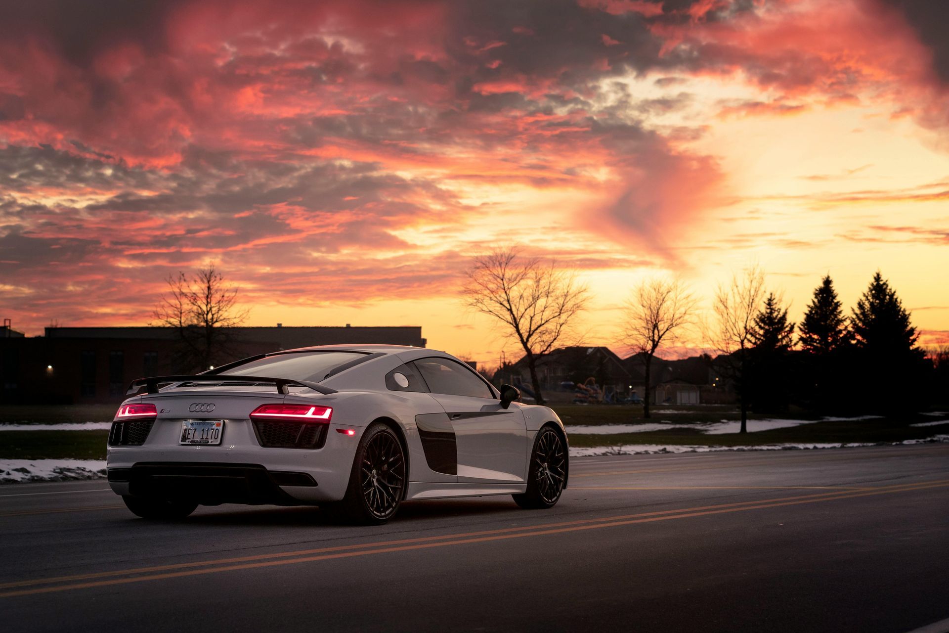 A white audi r8 is driving down a road at sunset.