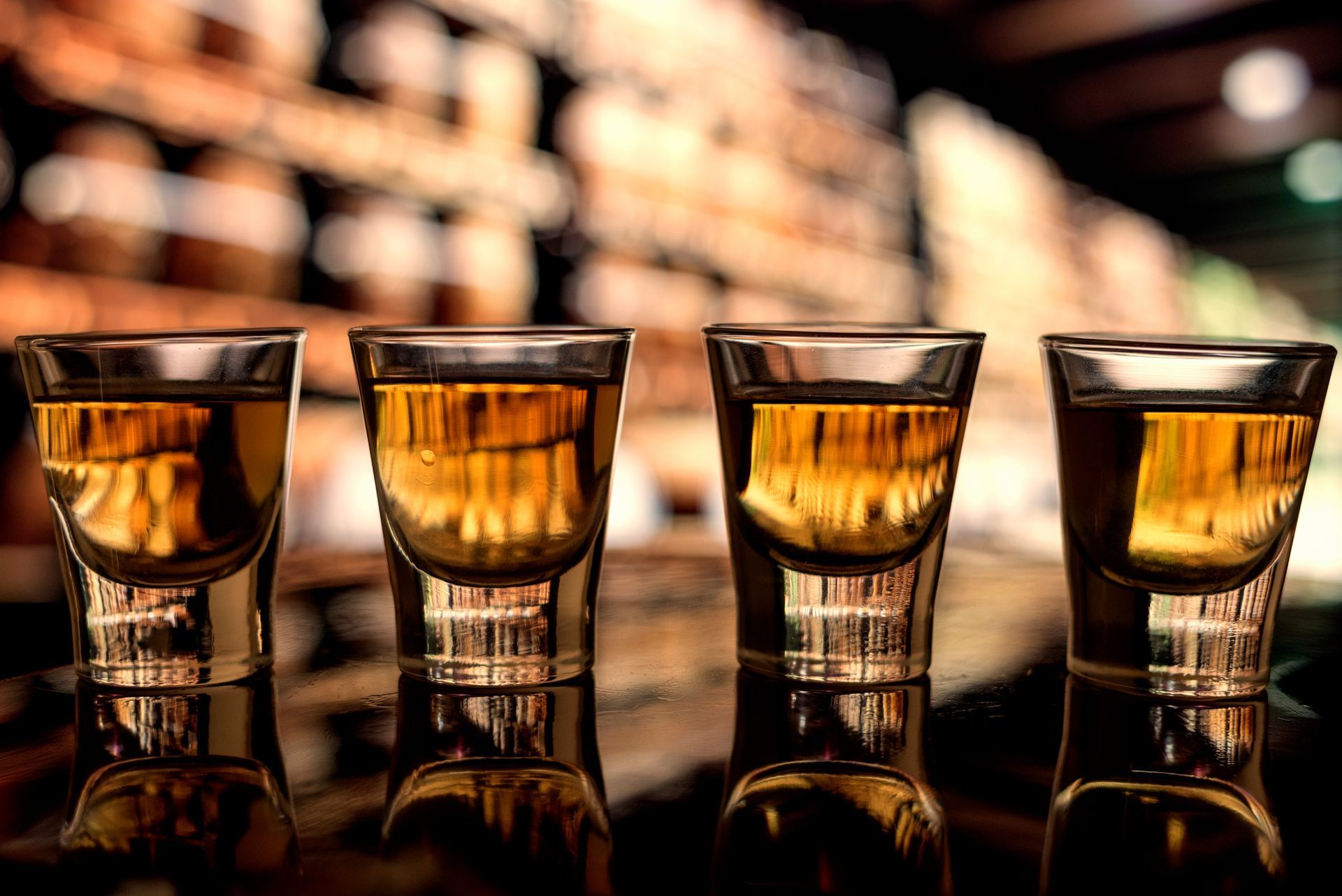 Four shot glasses filled with alcohol are lined up on a bar.