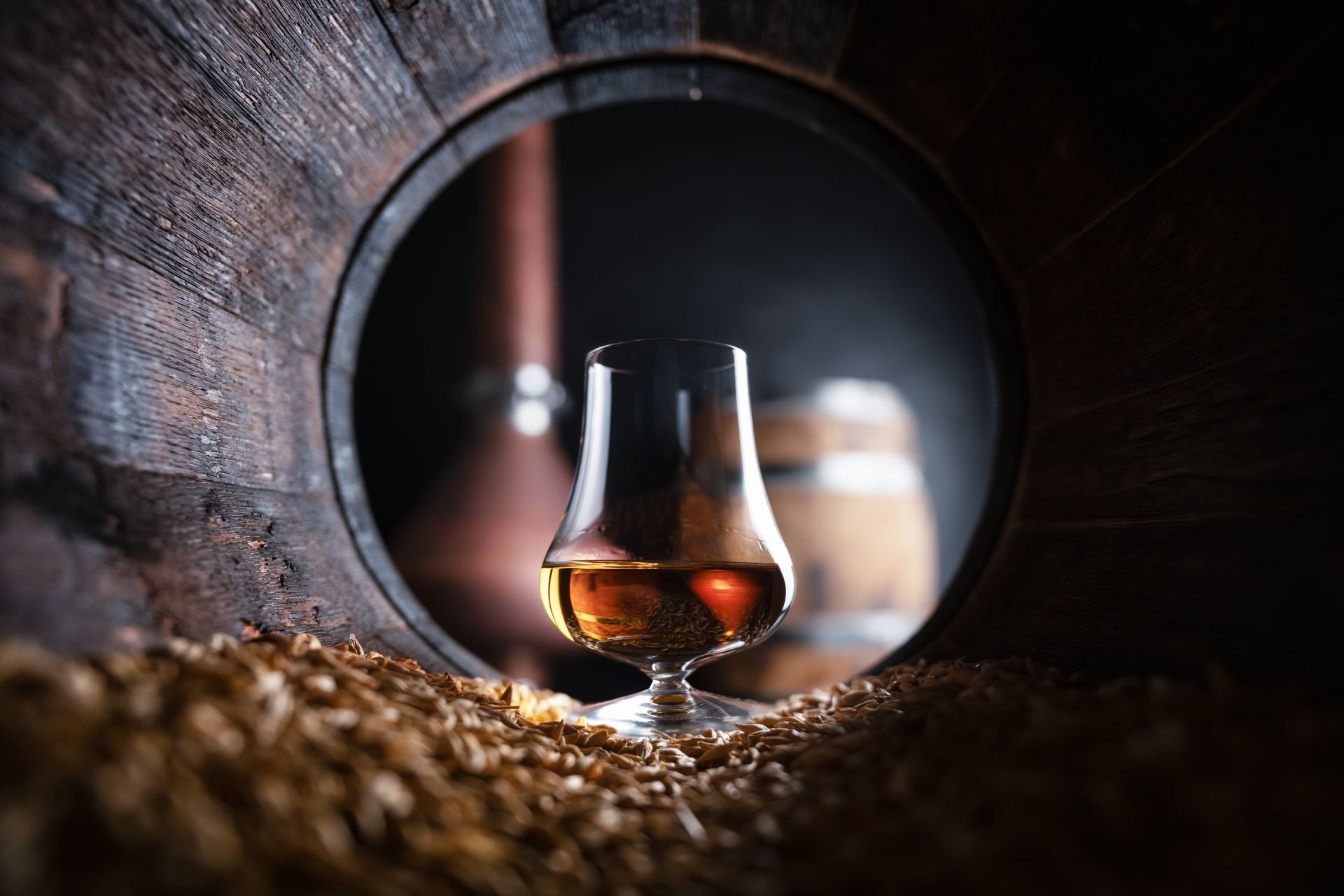 A glass of whiskey is sitting inside of a wooden barrel.