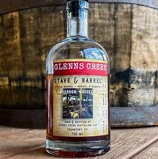A bottle of bourbon whiskey is sitting on a wooden table next to a wooden barrel.
