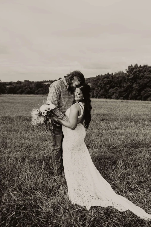 A bride and groom are posing for a black and white photo in a field.