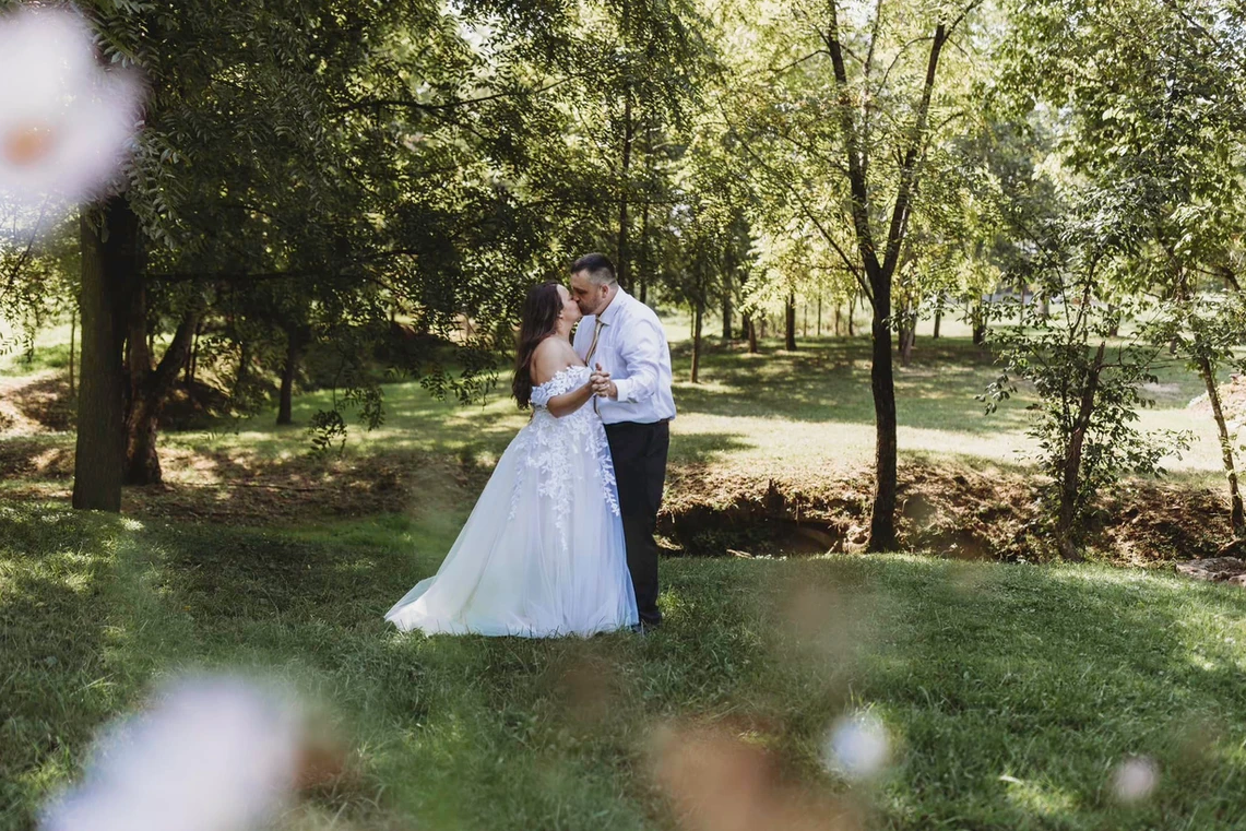 A bride and groom are kissing in the grass in a park.