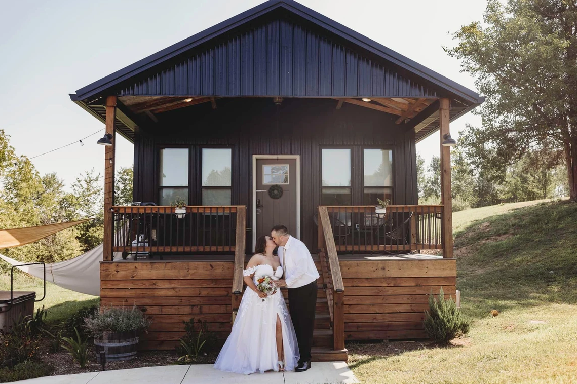 A bride and groom are kissing in front of a small black house.