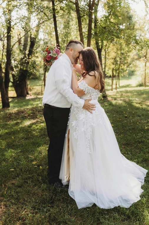 A bride and groom are kissing in the grass.