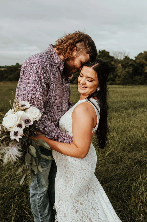 A bride and groom are posing for a picture in a field.