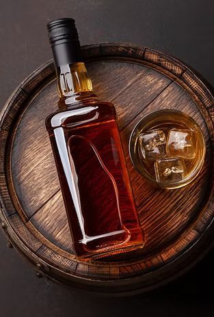 A bottle of whiskey and a glass of whiskey on a wooden barrel.