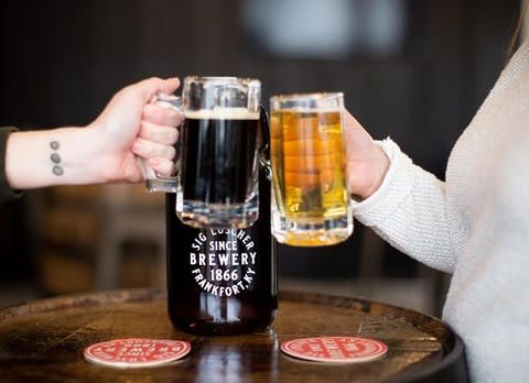 Two people are toasting with beer mugs on a table.