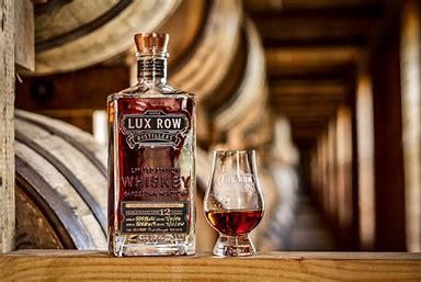 A bottle of lux row whiskey next to a glass of whiskey.