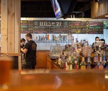 A man is standing behind a bar in a restaurant.