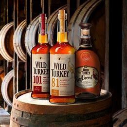 Three bottles of wild turkey whiskey are sitting on a wooden barrel