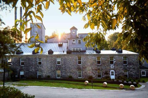 A large stone building with a metal roof is surrounded by trees and grass.