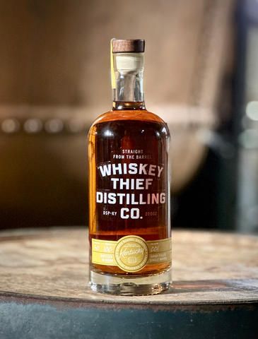 A bottle of whiskey is sitting on top of a wooden barrel.