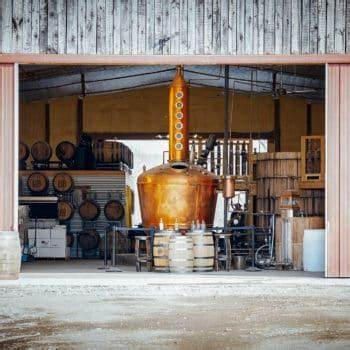 A large copper pot is sitting inside of a building next to barrels.