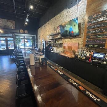 A long wooden bar in a restaurant with a tv on the wall.