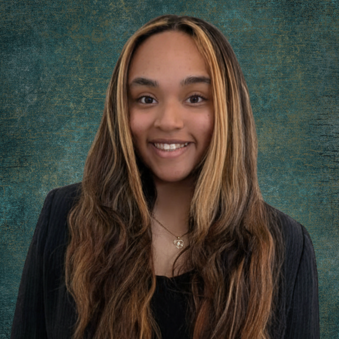 A man wearing glasses and a blue shirt is smiling in front of a brick wall