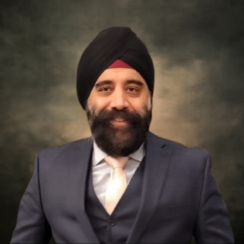 A man wearing glasses and a blue shirt is smiling in front of a brick wall