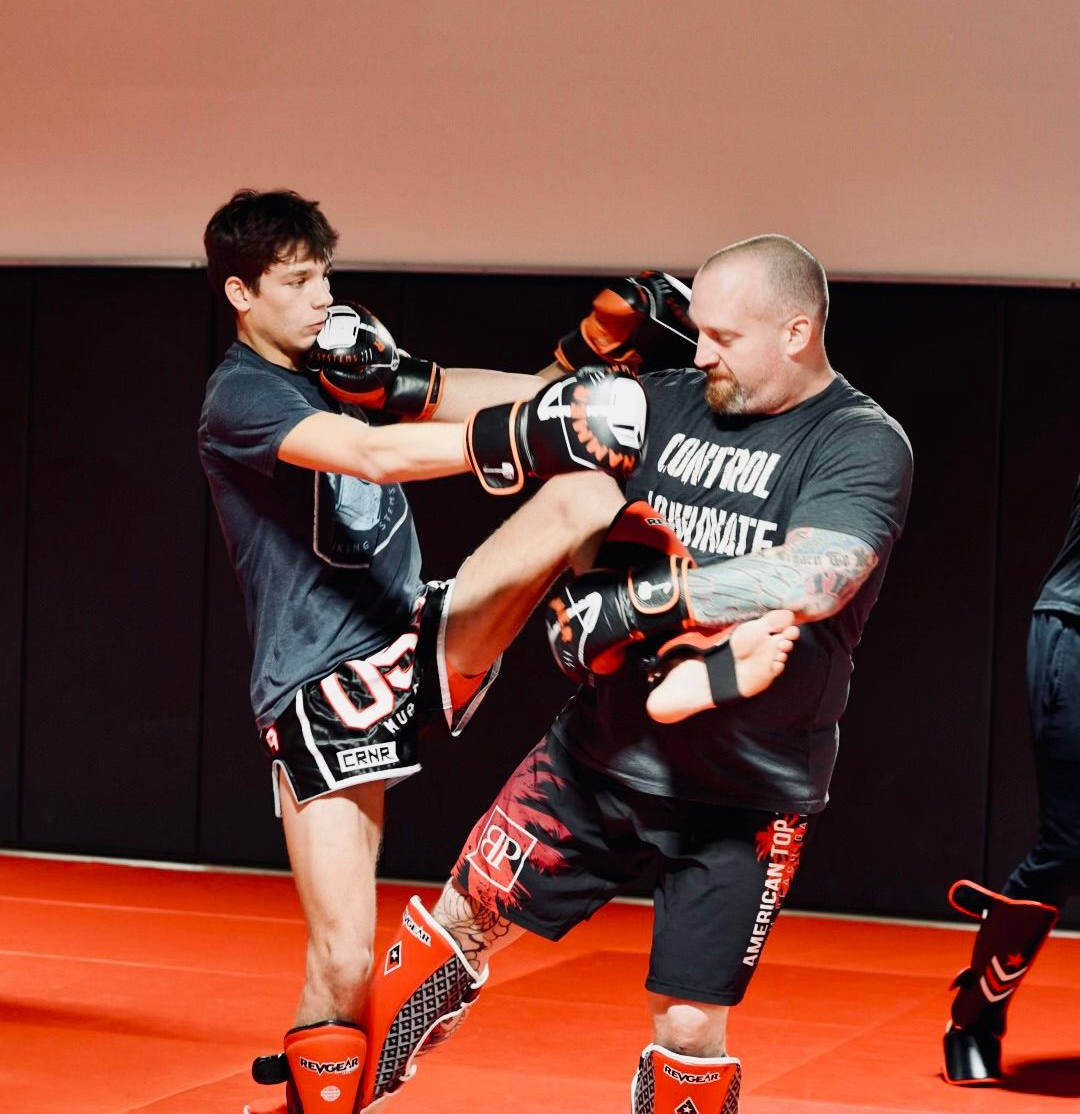 Three men are standing on a wrestling mat and one of them is wearing a yellow belt