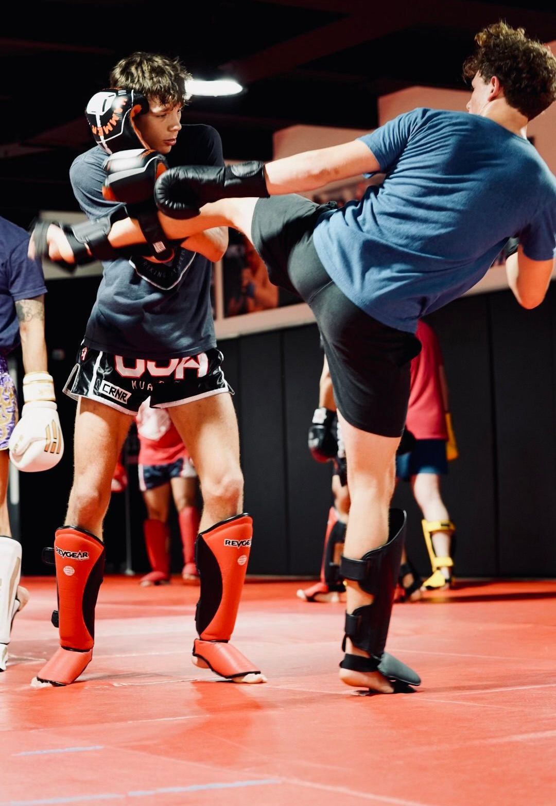 Three men are standing on a wrestling mat and one of them is wearing a yellow belt