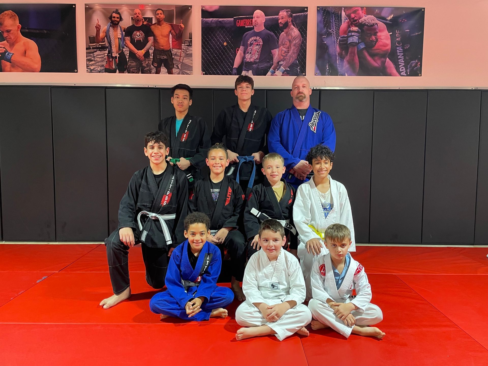 Three men are standing on a wrestling mat and one of them is wearing a yellow belt