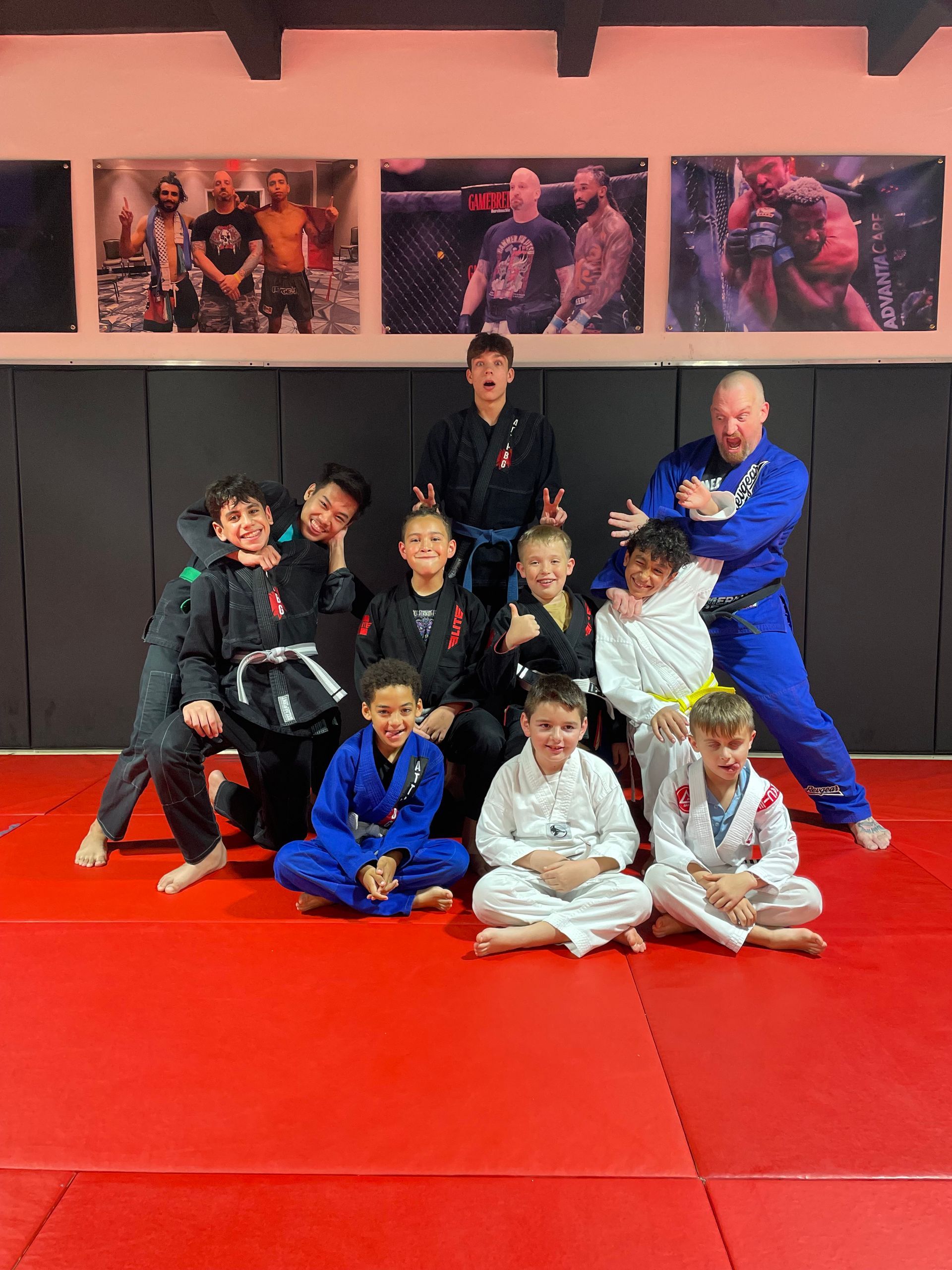 Three men are standing on a wrestling mat and one of them is wearing a yellow belt