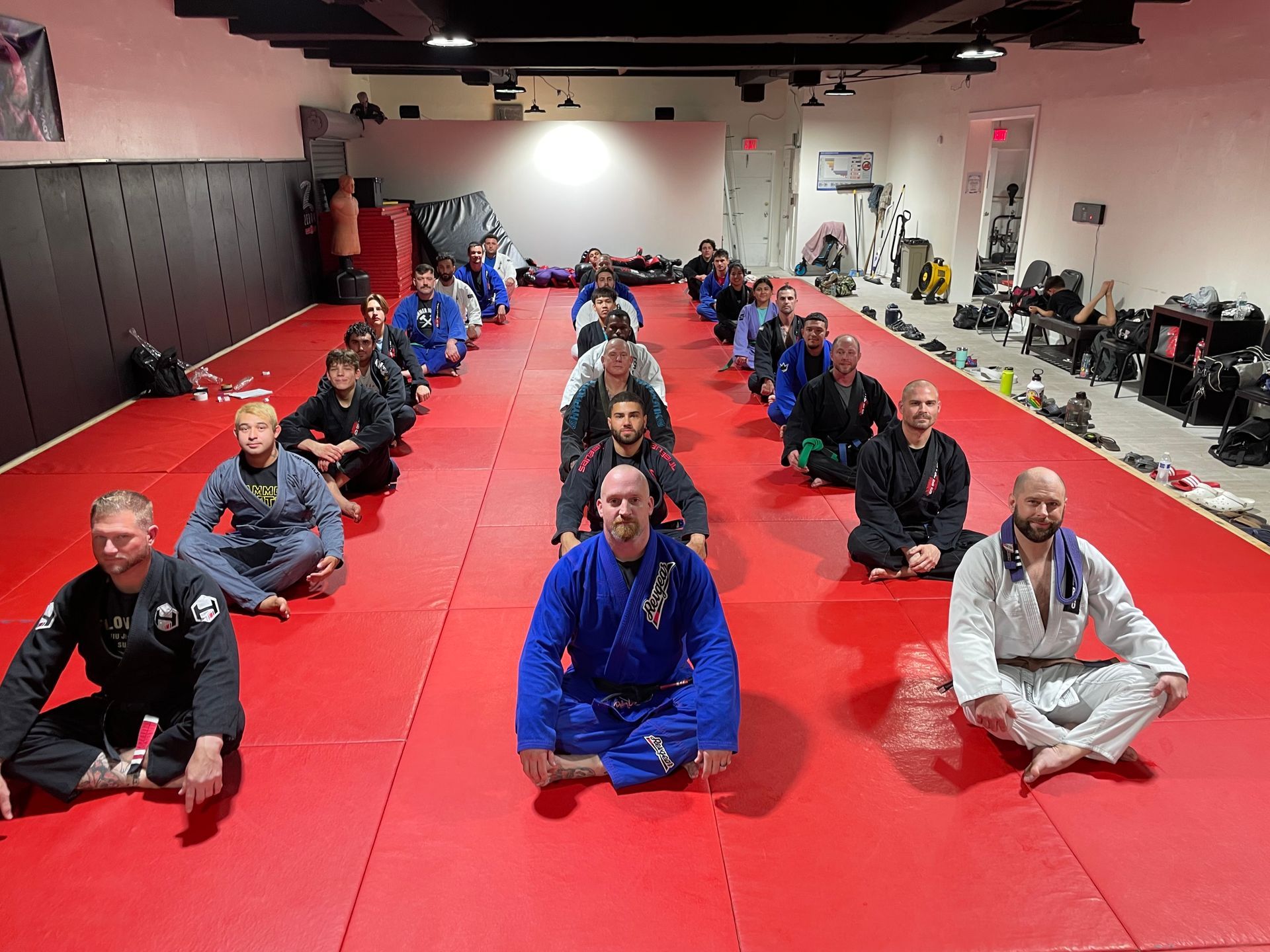 Three men are standing on a wrestling mat and one of them is wearing a yellow belt